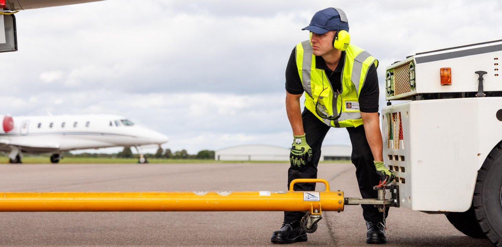 Ramp Agent wearing aviation PPE linking up a tow truck