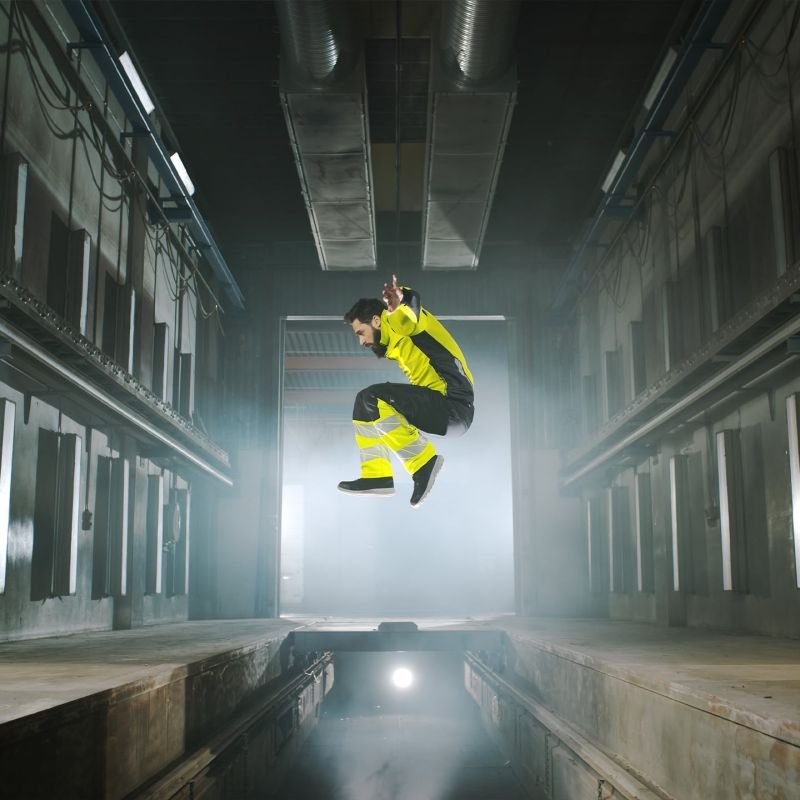 Model jumping in factory setting wearing black and yellow PPE