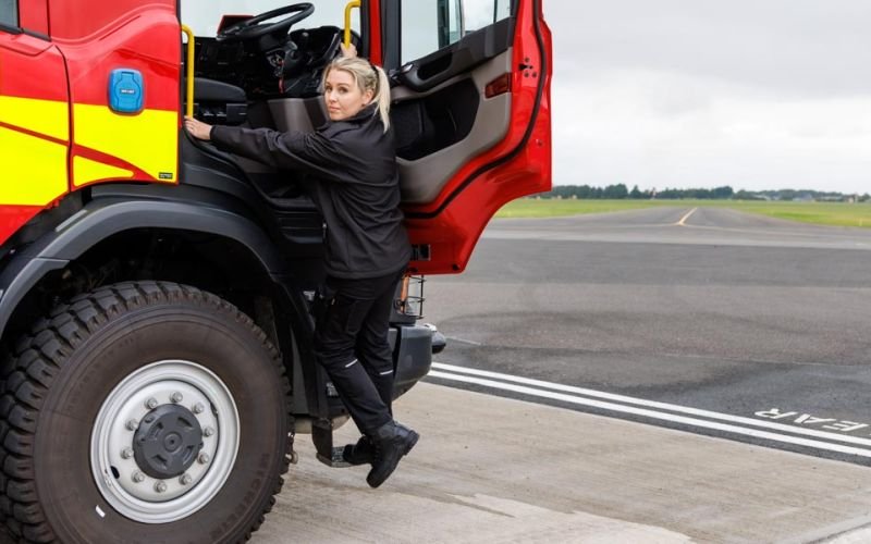 Female airport firefighter getting into fire engine